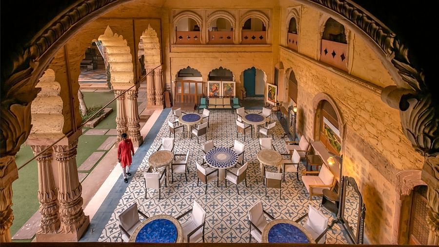View through an archway, the inner courtyard of Neemrana's Tijara Fort Palace features tables and chairs arranged on patterned tile flooring.