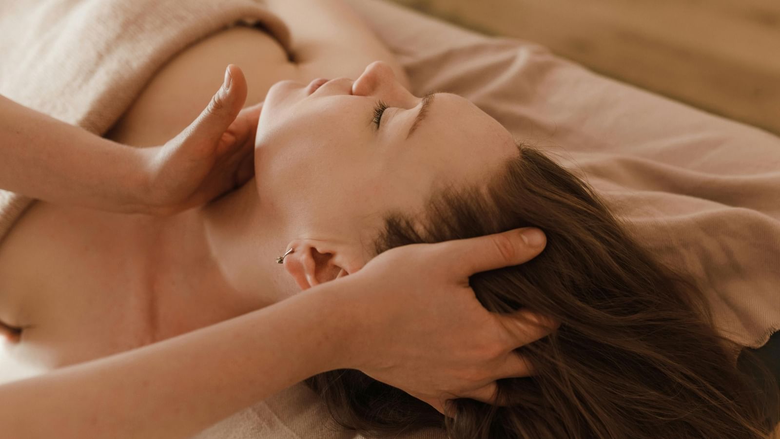  A client with her eyes closed lies on a massage table as a therapist gently massages her neck and head.