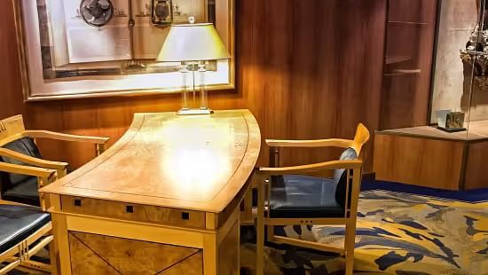 View of a Classic hotel workspace with a wooden desk, lamp, and framed artwork.