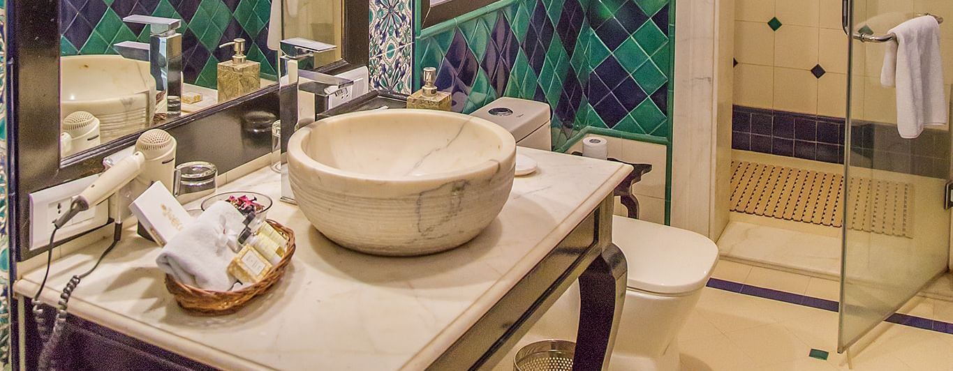 A bathroom at Royal Heritage Haveli with a decorative basin, mirror, and light-coloured patterned walls.