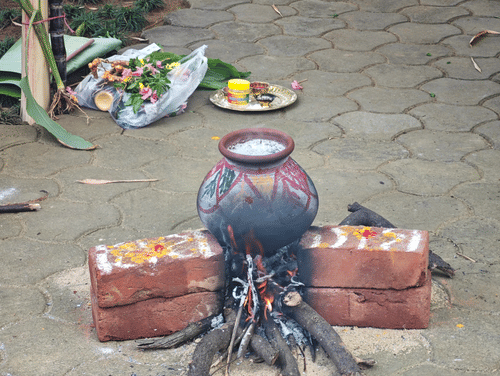 A clay pot set over an open fire, likely for cooking, with additional offerings and items arranged on the ground nearby, indicating a ceremonial or traditional activity.