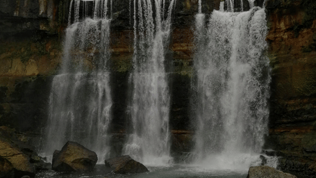 Waterfalls cascading over a rocky cliff into a pool surrounded by misty landscapes
