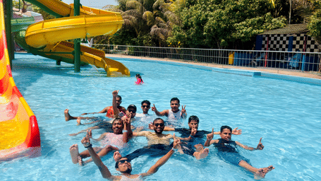 A group of people swimming together in an outdoor swimming pool near a yellow water slide.