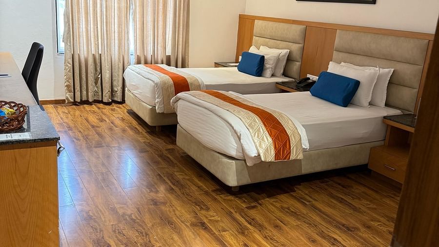 A wider shot of the Deluxe Twin With Breakfast room at Kyriad Hotel, Gulbarga, highlighting the two made beds, a window with sheer curtains, a desk, and framed artwork on the wall.