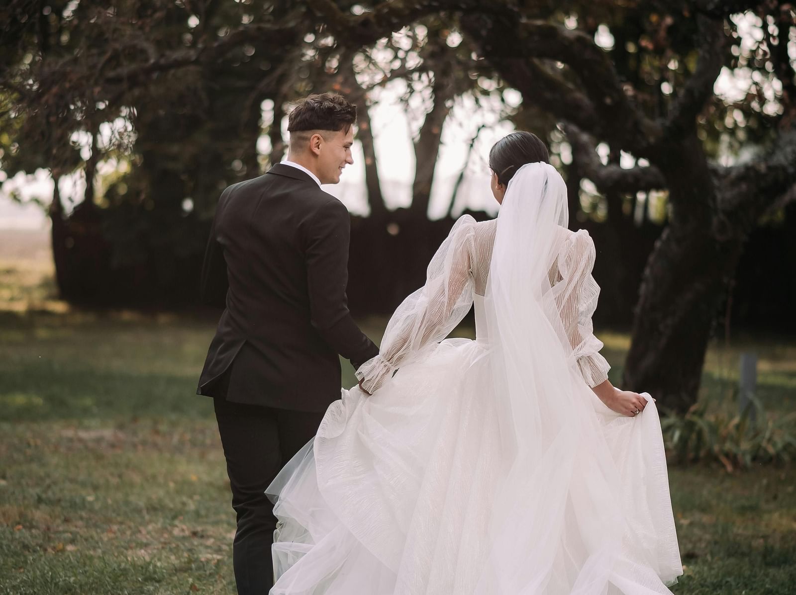 An image of a couple walking with their back towards the camera in a lush green setting