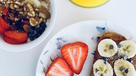 Top down view of a bowl of cereal placed beside a French toast and a glass of orange juice