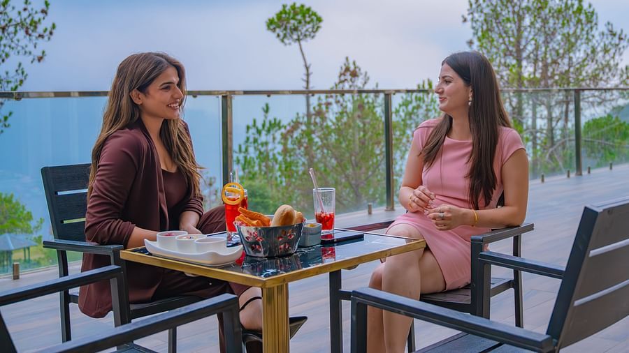 An image of two women talking to each other in a dining table which is set in the outdoors - An image of two women lying on a bed to receive massage - The Manor Luxury Hotel, Shimla