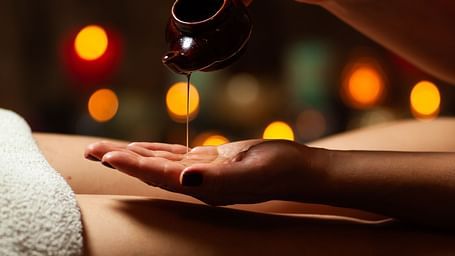 Hand pouring oil from a small pot onto a person’s hand.