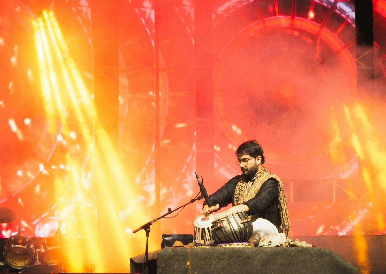 A musician is silhouetted on a stage, surrounded by bright red and orange stage lights.
