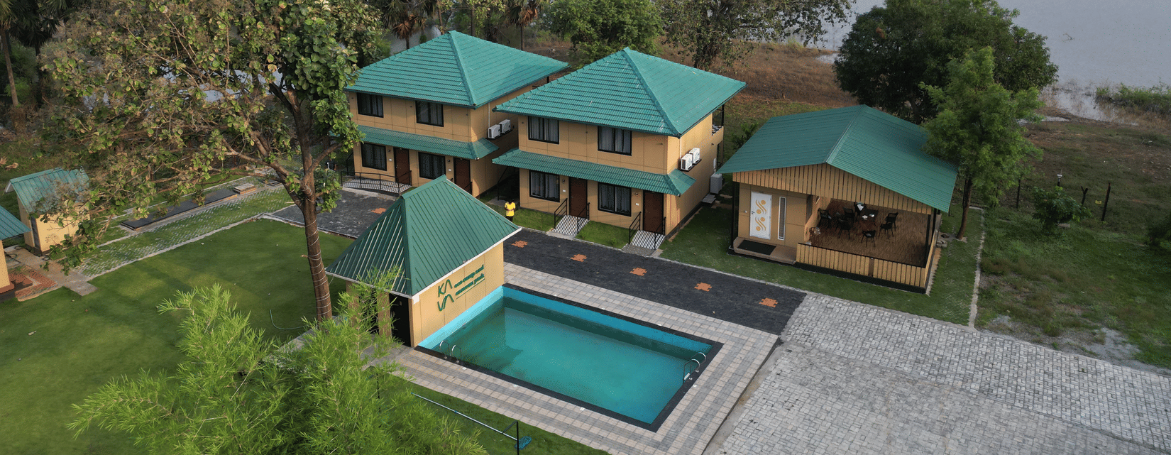 Wide daytime aerial shot of the resort complex situated on the banks of a peaceful lake surrounded by hills - Ibex Resorts, Malampuzha (Kava Eco Camp and Caravan Park)