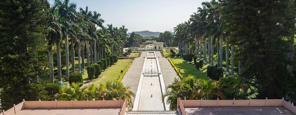 A scenic view of a garden with a long, winding pathway lined with trees and bushes. The garden is well-maintained and has a peaceful atmosphere.