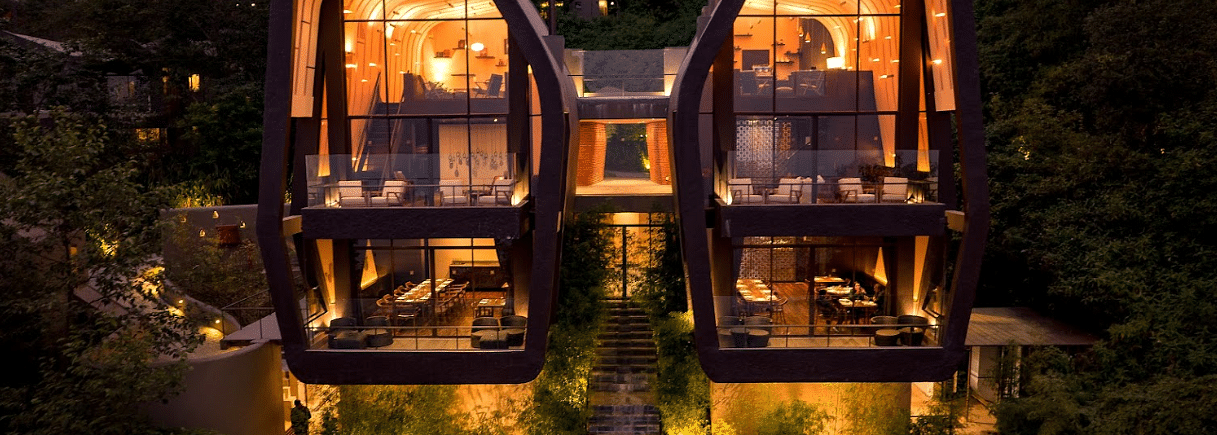 A front view of two individual beautifully lighted villas | A bedroom with large window giving a view of a sitting area on the deck | Kavya Resort and Spa, Nagarkot