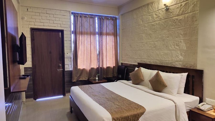Bedroom with a huge bed, bedside table, windows with curtains, wooden door, and a TV | Standard Room | Woodstock Resorts, Coorg