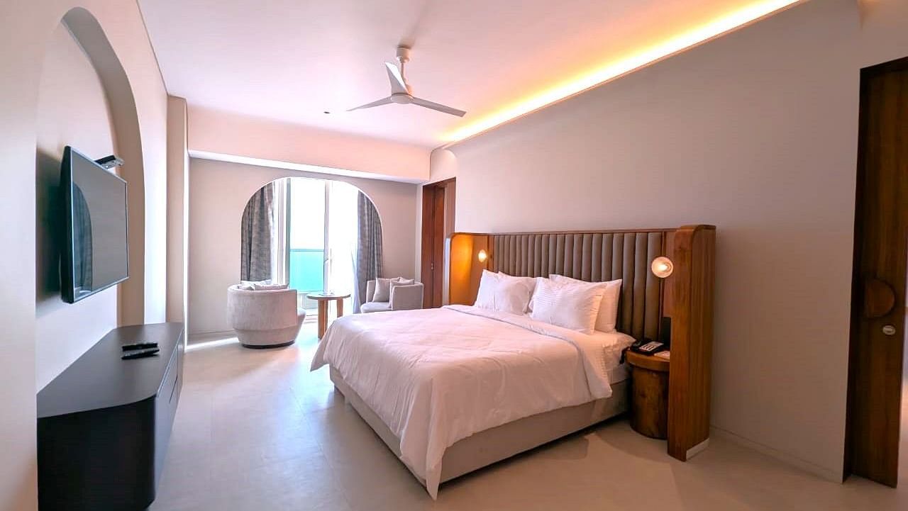 A corner view of the bedroom at Swosti Premium Beach Resorts, Puri, with a made bed, ceiling fan, and television.