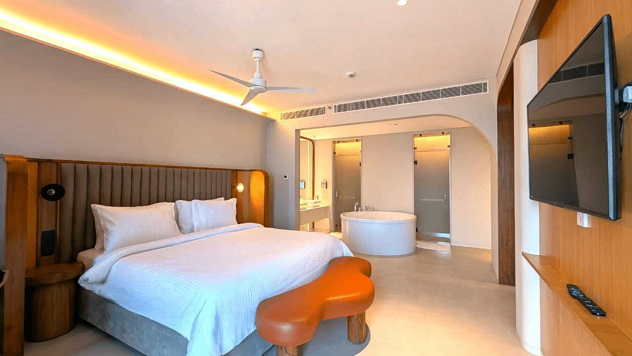 A bedroom at Swosti Premium Beach Resorts, Puri, with a made bed, wooden accents, and a view into the bathroom area.