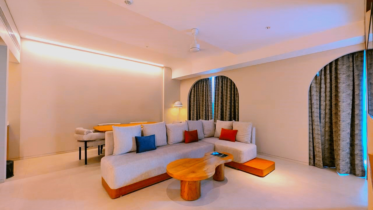 A bedroom and living area at Swosti Premium Beach Resorts, Puri, with a made bed, colorful seating, and an arched doorway.