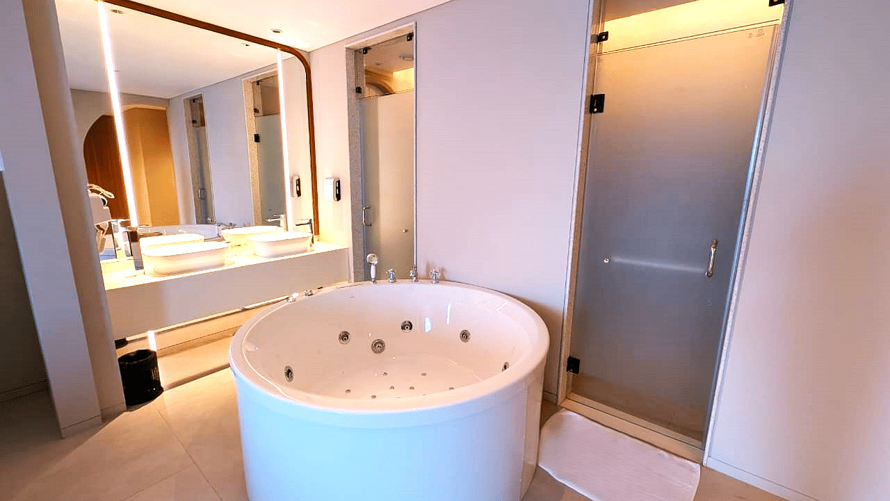 A bathroom at Swosti Premium Beach Resorts, Puri, featuring a unique, cylindrical bathtub and a mirrored cabinet.
