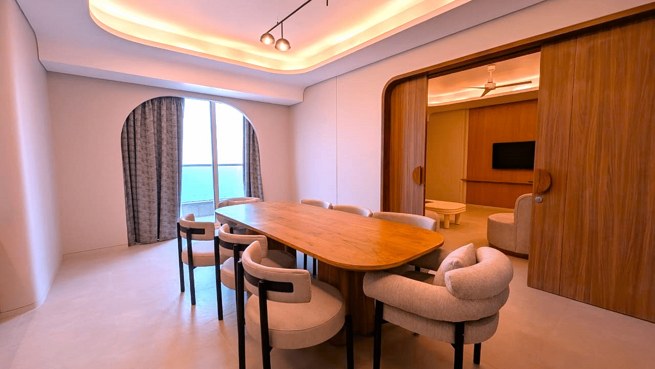 A dining area at Swosti Premium Beach Resorts, Puri, with a wooden table and chairs, and a view of the window.