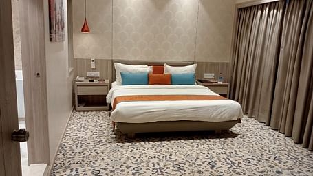A contemporary hotel bedroom featuring a large bed with white bedding, decorative cushions, and warm ambient lighting.