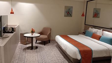 Modern hotel room with twin beds, a small table and chair, soft lighting, and minimalist decor.