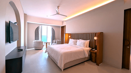 A corner view of the bedroom at Swosti Premium Beach Resorts, Puri, with a made bed, ceiling fan, and television.