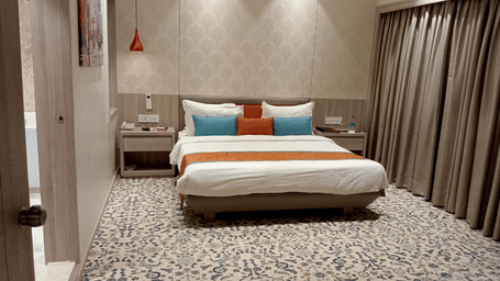 a contemporary hotel bedroom featuring a queen size bed, bedside tables, a ceiling-to-floor windows, and a door opening to the washroom at Lords Inn Rajkot