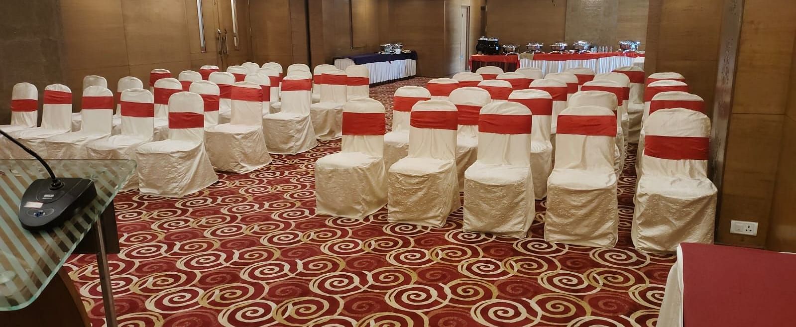An event space in a hotel with banquet seating and decorative carpet.- The President Hotel Jayanagar, Bangalore