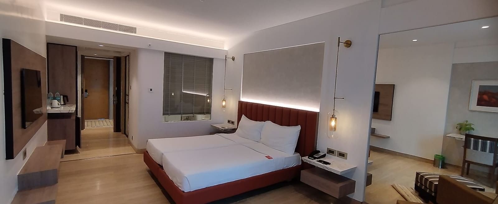 A well furnished executive bedroom in Mirage Hotel, featuring twin beds, a large mirror, and a wooden panelled entertainment unit.