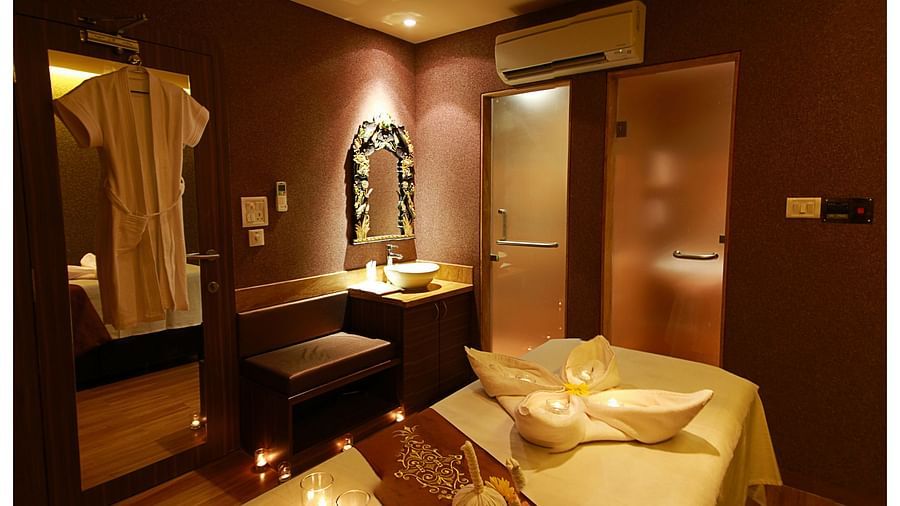 a massage table with things kept on it and a robe hung on the mirror - IOSIS Spa & Wellness