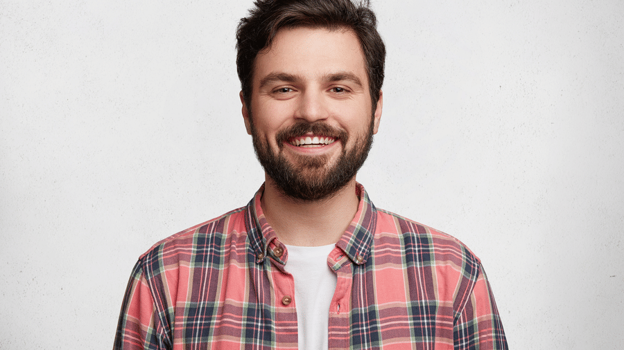 Man with a beard wearing a red and white checkered shirt, smiling.