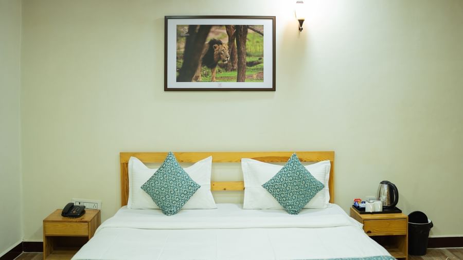 A view of the bed with blue accents, a wall art, and bedside tables at Daksh Resort & Amusement Park, Sasan Gir.