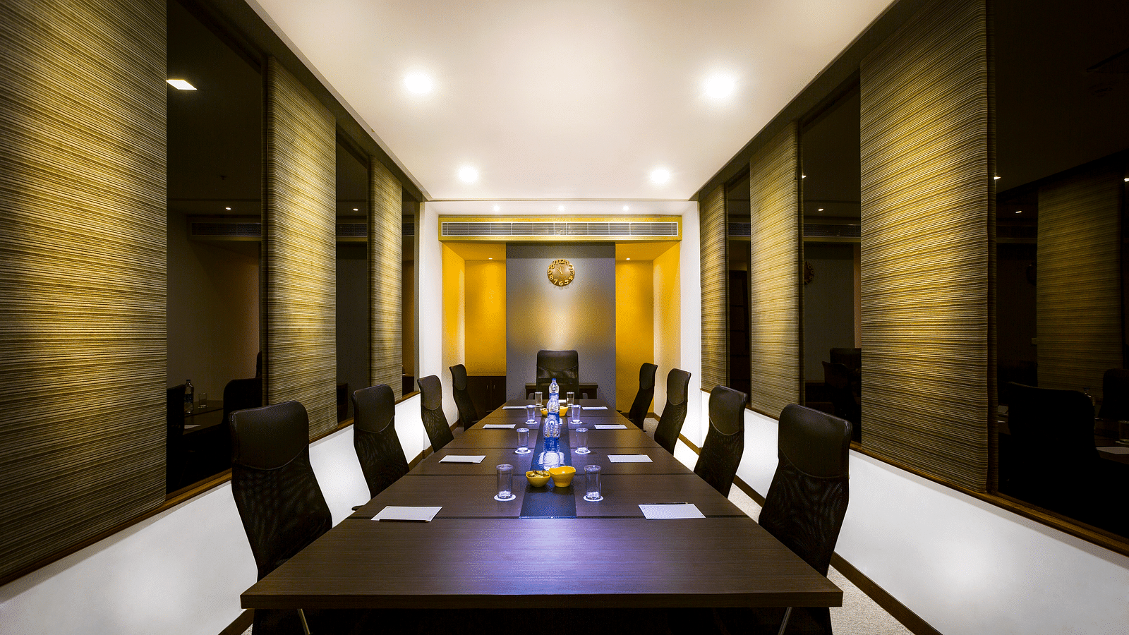 Modern meeting room with a long, rectangular table surrounded by black leather chairs. The room has neutral walls and ample lighting.