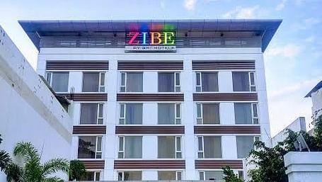 Facade shot of zibe hotel where cars are parked in the front.