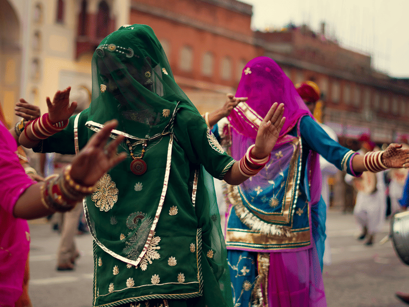 Women in vibrant Rajasthani ghagras dance through Jaipur street, colourful veils swirling