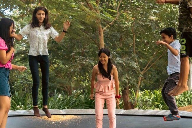 Children playing on a trampoline while adults watch from nearby under the shade of trees at Karma Chalets.