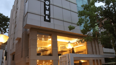 Exterior view of a contemporary multi-storey hotel building at dusk, featuring a glass facade, lit signage, and a paved entrance area at Emblem Hotel, New Friends Colony, New Delhi.