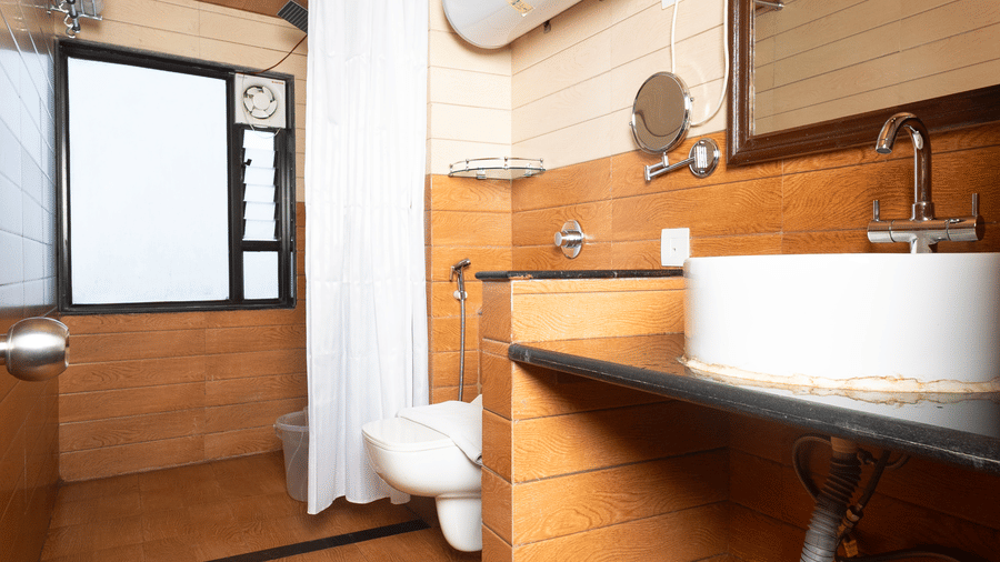 Stylish wash basin area at Sumitel Hotels featuring a modern round sink, large mirror, wooden and white panel walls, sleek countertop, and warm ambient lighting.