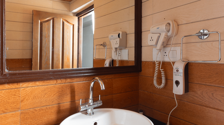 Stylish wash basin area at Sumitel Hotels featuring a modern round sink, large mirror, wooden and white panel walls, sleek countertop, and warm ambient lighting.