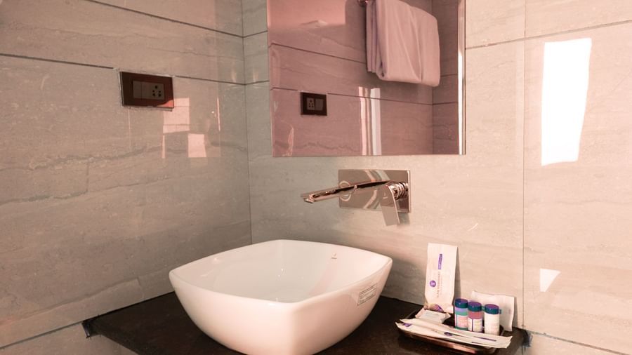 Bathroom at Sumitel Premier Inn, Siliguri, with a wash basin, wall mirror, and modern fittings set against tiled walls for guest convenience.
