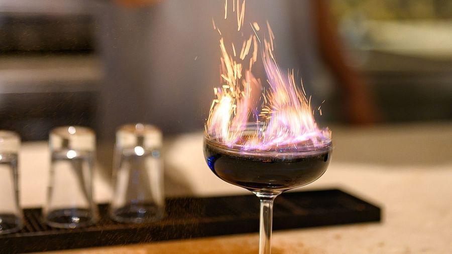 A bartender sprinkling salt on a fiery drink; the bartender seen in the backdrop - Maikhao Dream Villa Resort & Spa, Phuket