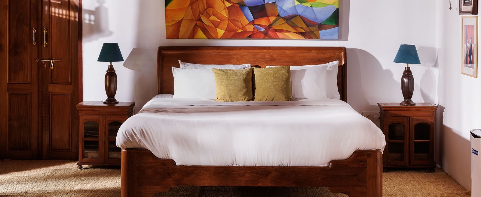 A close up shot of a bed, bedside tables, lamps and a painting hung on the wall at BluSalzz Villas - Muhamma Resort, Alleppey