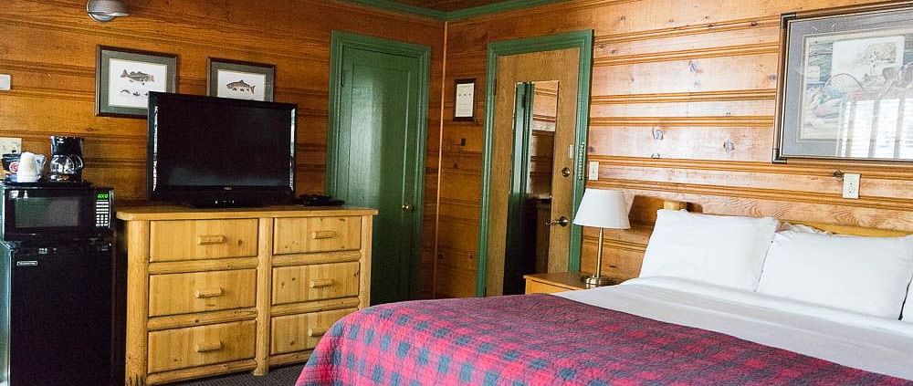 A room with a double bed, a wooden cabinet with a TV placed on it and a ceiling fan with a light at Shaver Lake Village Hotel.