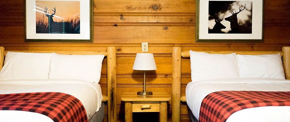 A wooden cabin with twin beds and a side table with a night lamp placed between them at Shaver Lake Village Hotel.