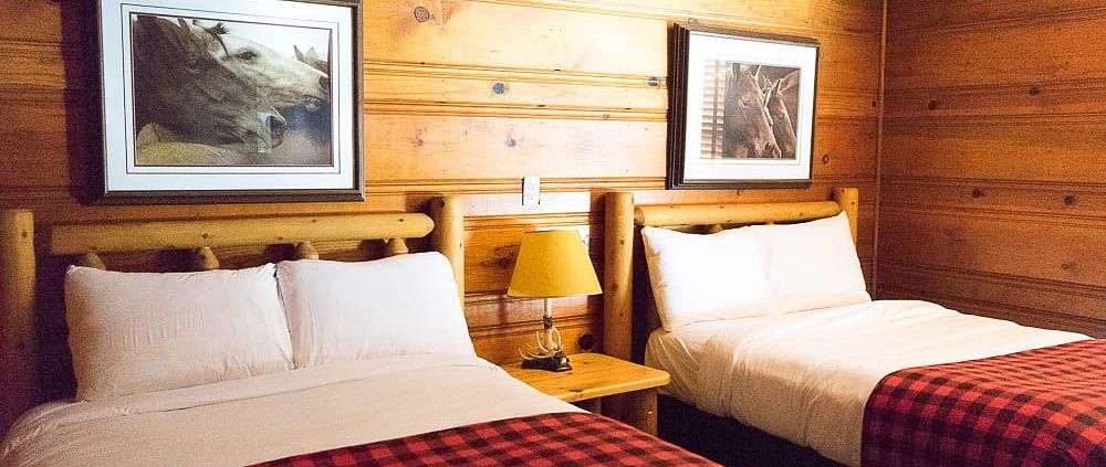 A wooden cabin with twin beds with photographs hung on the wall behind them at Shaver Lake Village Hotel.