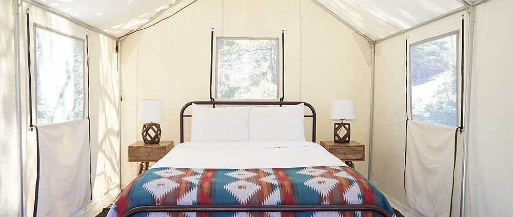 A tent with zip-down windows and a double bed placed in the middle at Shaver Lake Village Hotel.