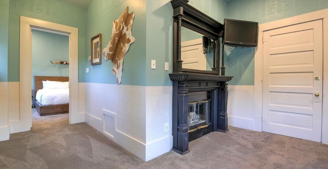 he Groveland Hotel's living area showcases sage green walls, an ornate black fireplace, mounted TV, and distinctive animal hide wall decor.