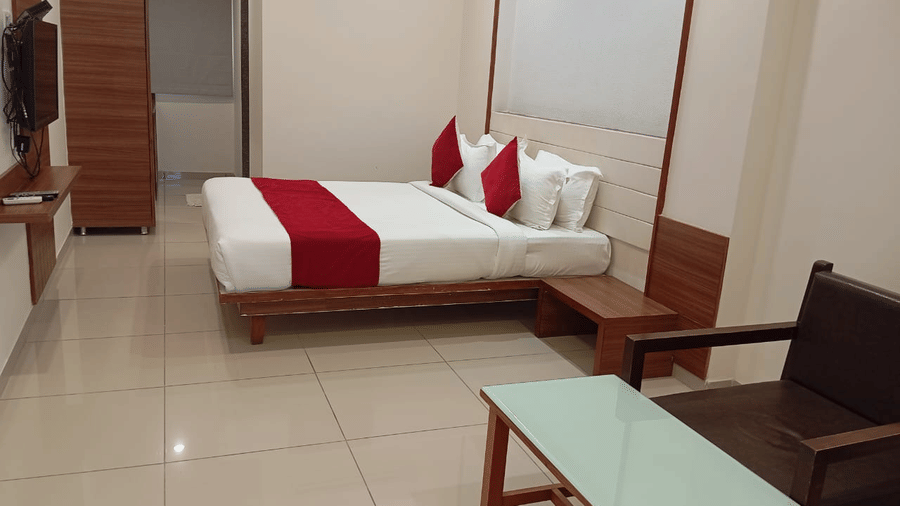 A Deluxe Room at Hotel Ashray Inn Express featuring a large bed, bedside tables, seating area with chairs and center table, wardrobe, and tiled flooring.