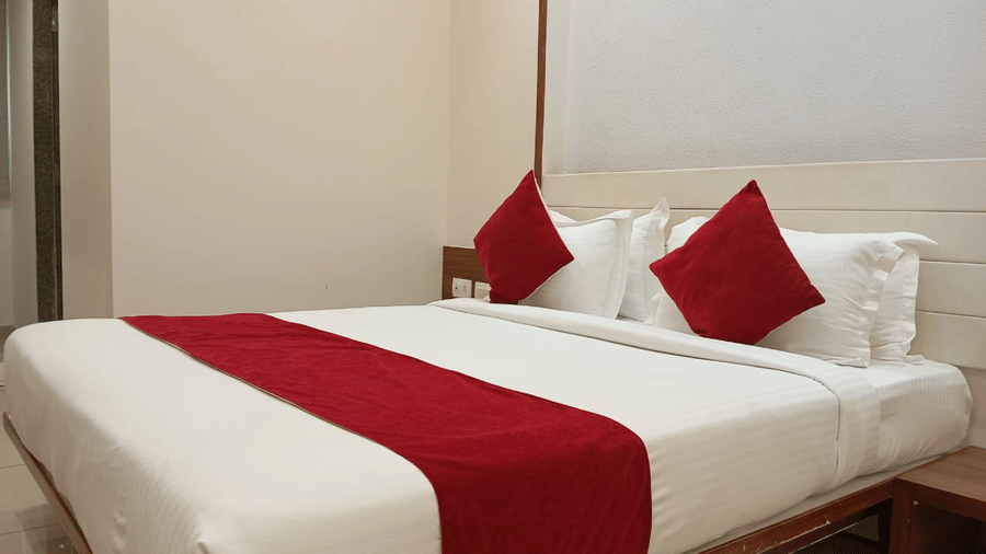 A Deluxe King Room at Hotel Ashray Inn Express showcasing a spacious bed with accent cushions, wooden headboard, bedside lighting, and minimalist interiors.