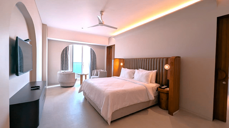 A corner view of the bedroom at Swosti Premium Beach Resorts, Puri, with a made bed, ceiling fan, and television.