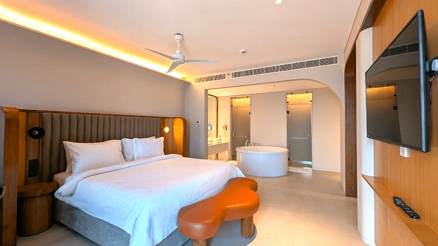 A bedroom at Swosti Premium Beach Resorts, Puri, with a made bed, wooden accents, and a view into the bathroom area.
